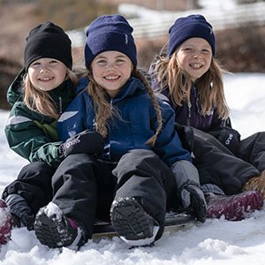 Tre glada barn som sitter i snön med Gneis vinterkläder på sig