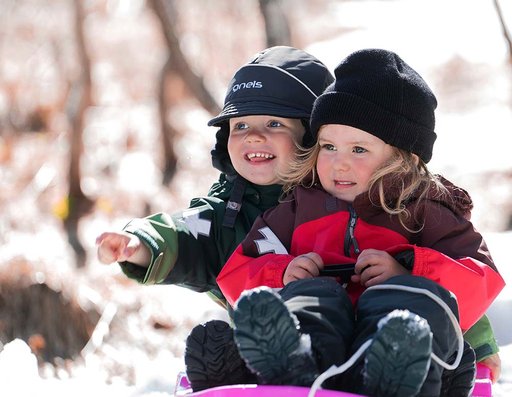 Två små barn som åker pulka och har på sig Minishape - Gneis vinteroverall för de minsta