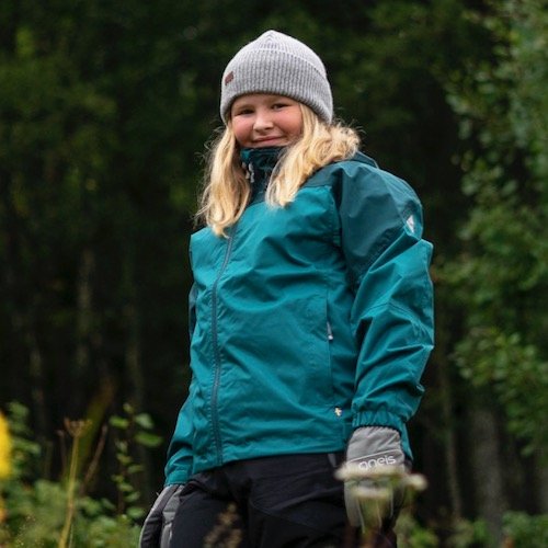 En tjej som står i skogen med Gneis Speed Shell skaljacka på sig