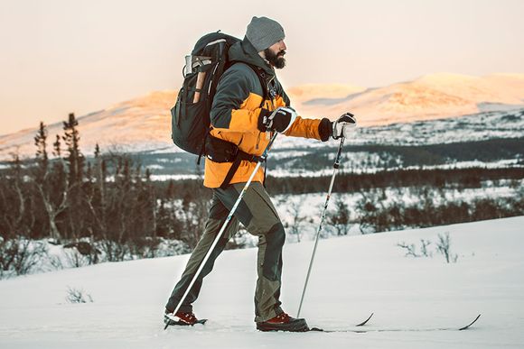 En kille åker längdskidor på fjället med outdoorkläder som är orange och svarta