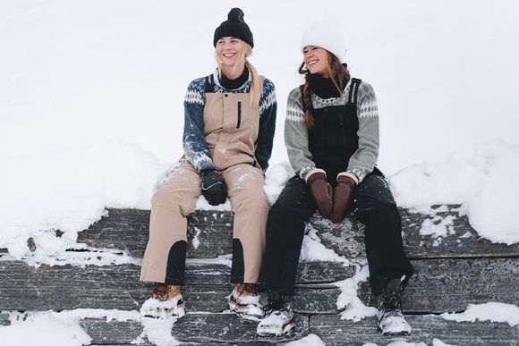 Två tjejer sitter på en snöig mur tillsammans med varma och bekväma byxor som tål snö och vind