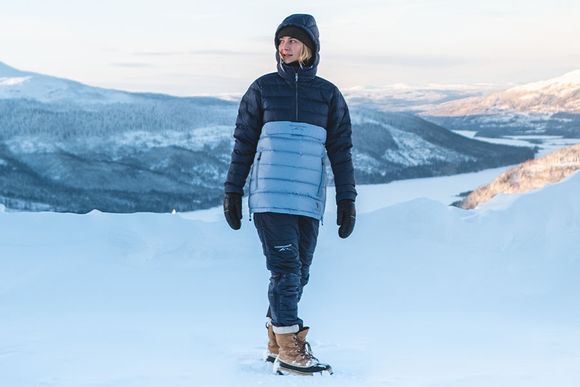 En tjej står på snötäckta berg med en varmjacka ifrån Swedemount kollektionen Östersund i färgen blå