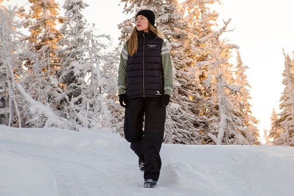 En tjej ute i vintrigt miljö med svarta och gröna outdoorkläder på sig ifrån Swedemount 