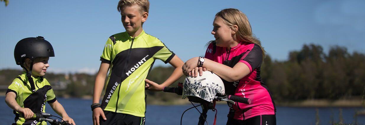 Tre barn/ juniorer som cyklar med grön/gula preformance cykelkläder ifrån Swedemount
