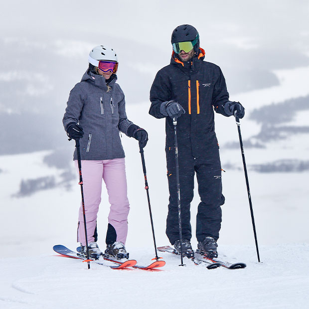 Ein Paar trägt die Bestseller schwarze Jacke sowie Skihosen in blau und rosa von St.Anton und Cervinia.