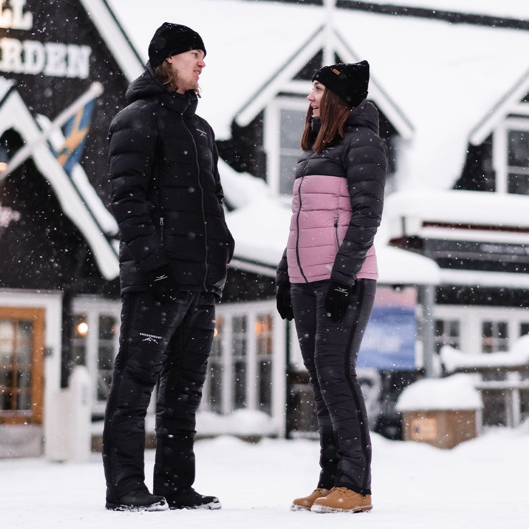 Mann und Frau stehen in schwarzen und schwarz-rosanen Winterjacken von Swedemount im Schnee.
