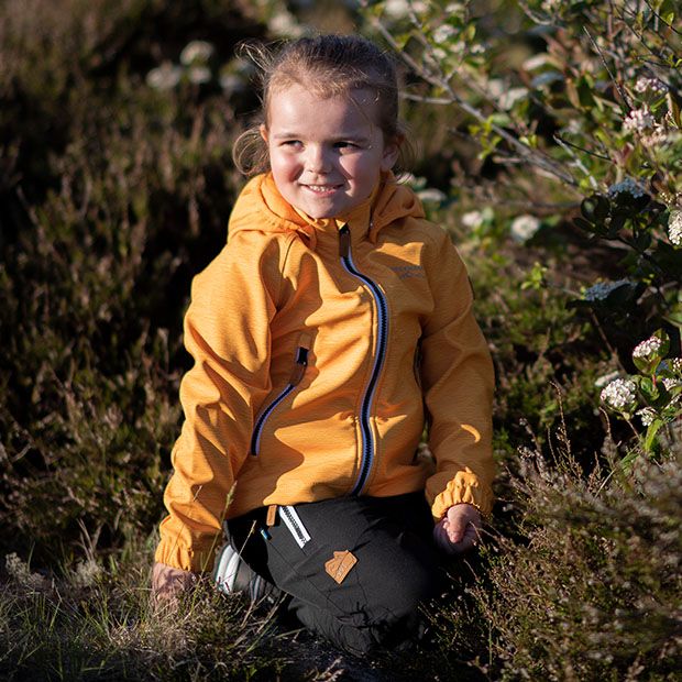 Ett barn som sitter i skogen med en gul jacka från Swedemount