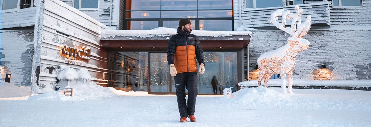 En kille står ute i snön med en orange och svart jacka ifrån Swedemount med kollektionen Östersund