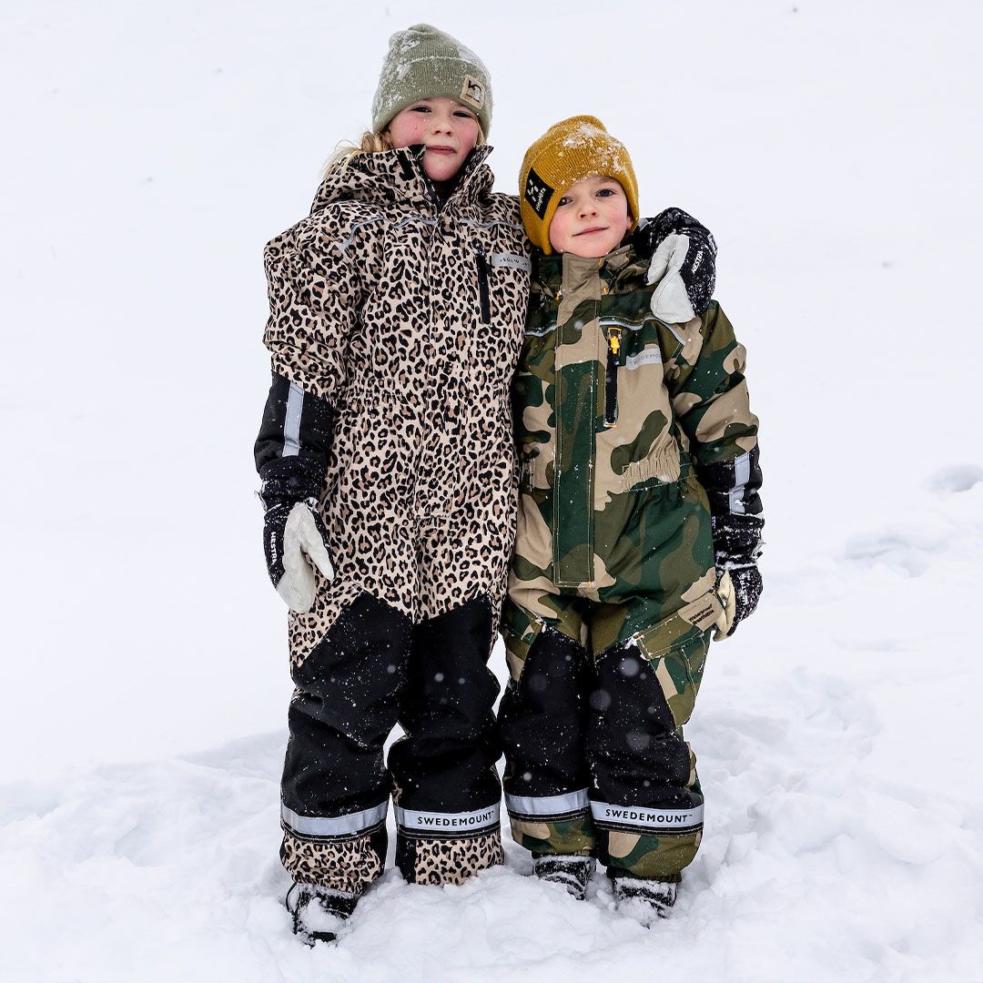 Ein Mädchen und ein Junge in gemusterten Kinderschneeanzügen, die eine in Leo-Muster, der andere in Camouflage.