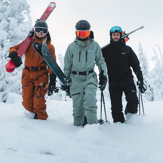 Drei Personen tragen Skianzüge von Swedemount in orange, türkis und schwarz im Schnee.